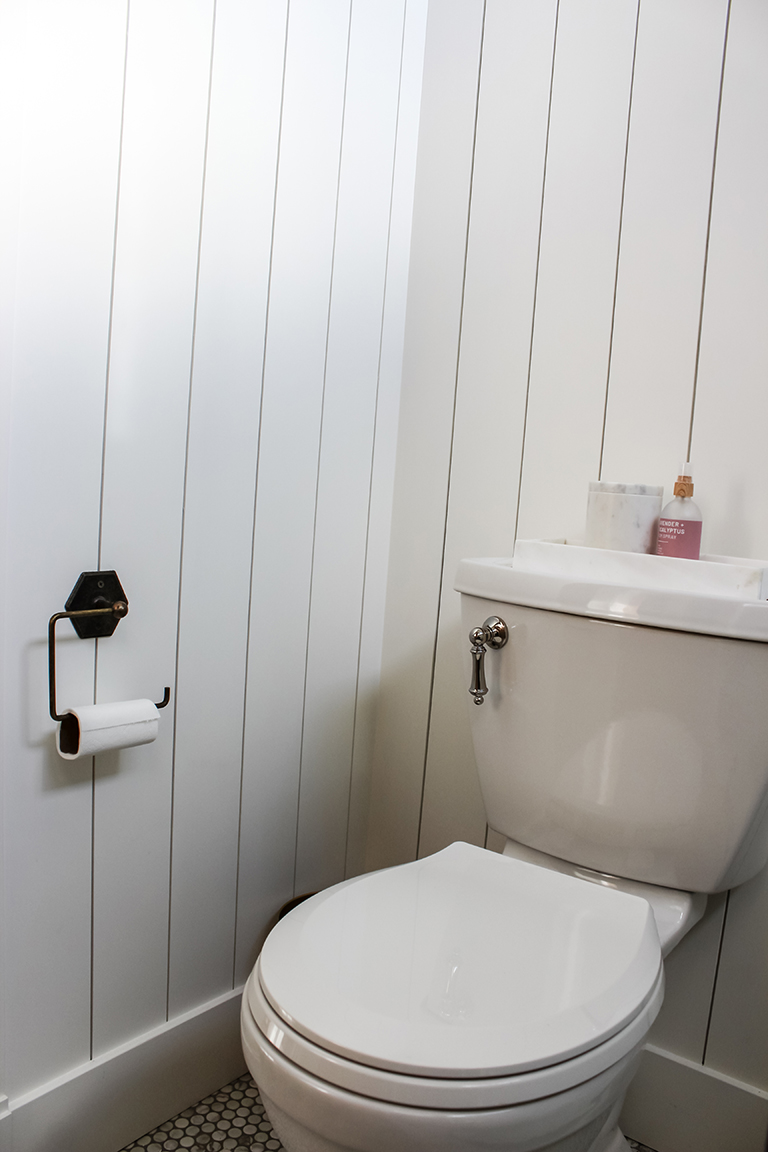Vertical shiplap bathroom walls marble tank tray and penny tile floors, polished nickel toilet tank lever, antique brass tp holder from hobby lobby.