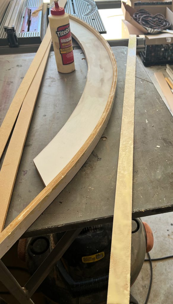1/4" mdf board has glue spread all along it ready for it to be nailed to the archway trim. the 1/4" thickness mdf is easily bendable to mold itself along the perimeter of the arch.