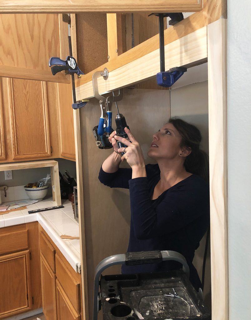 favorite tools for joinery are clamps and a kreg jig make drilling pocket holes an easy venture with any standard drill. Joannie is holding a drill and joining a piece of trim around a refrigerator opening