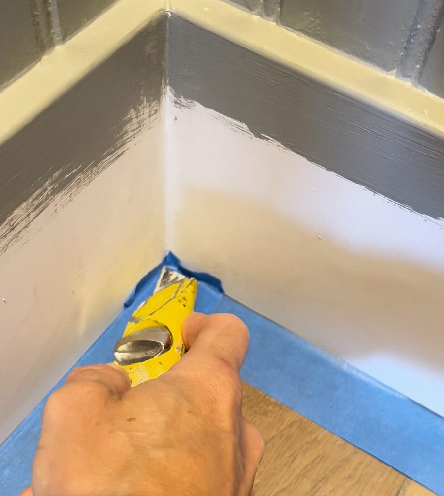Joannie positions a fixed blade utility knife in the corner of a baseboard to remove excess painter's tape before painting.